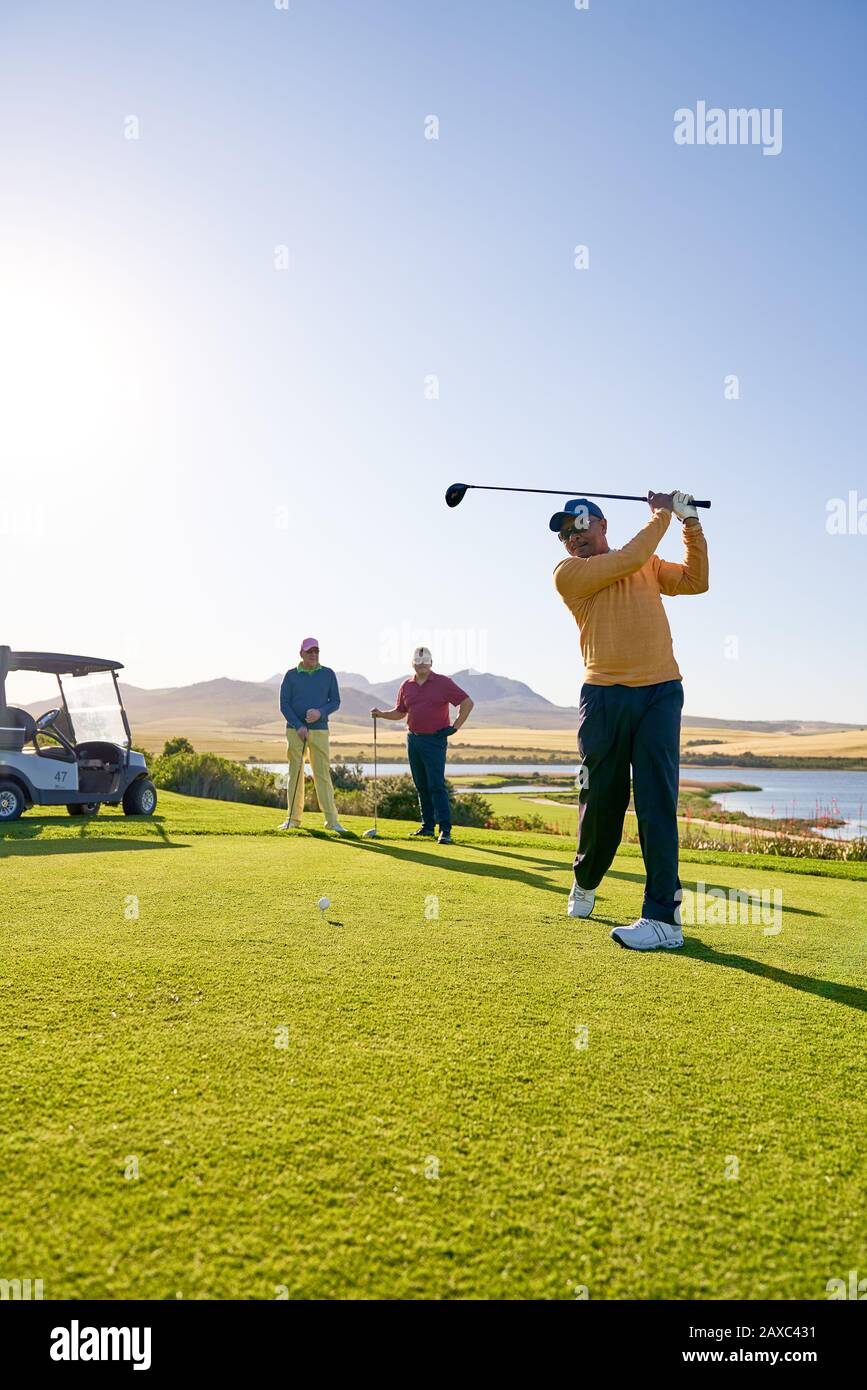 Male golfer teeing off at sunny golf course tee box Stock Photo