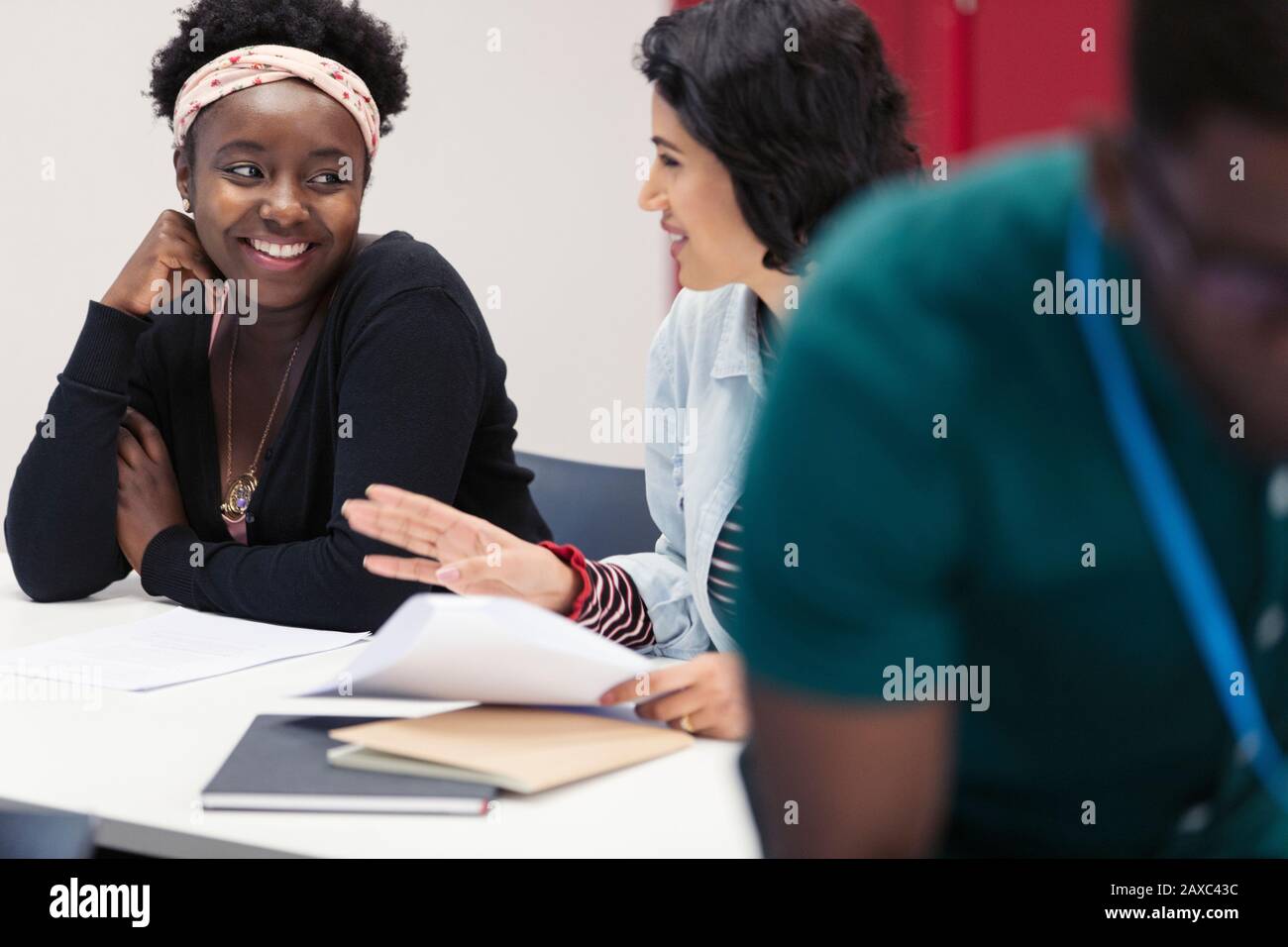 Smiling female community college students discussing paperwork in classroom Stock Photo