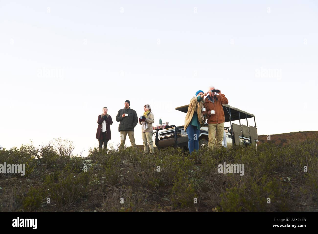 Safari tour group drinking tea and using binoculars on hill Stock Photo