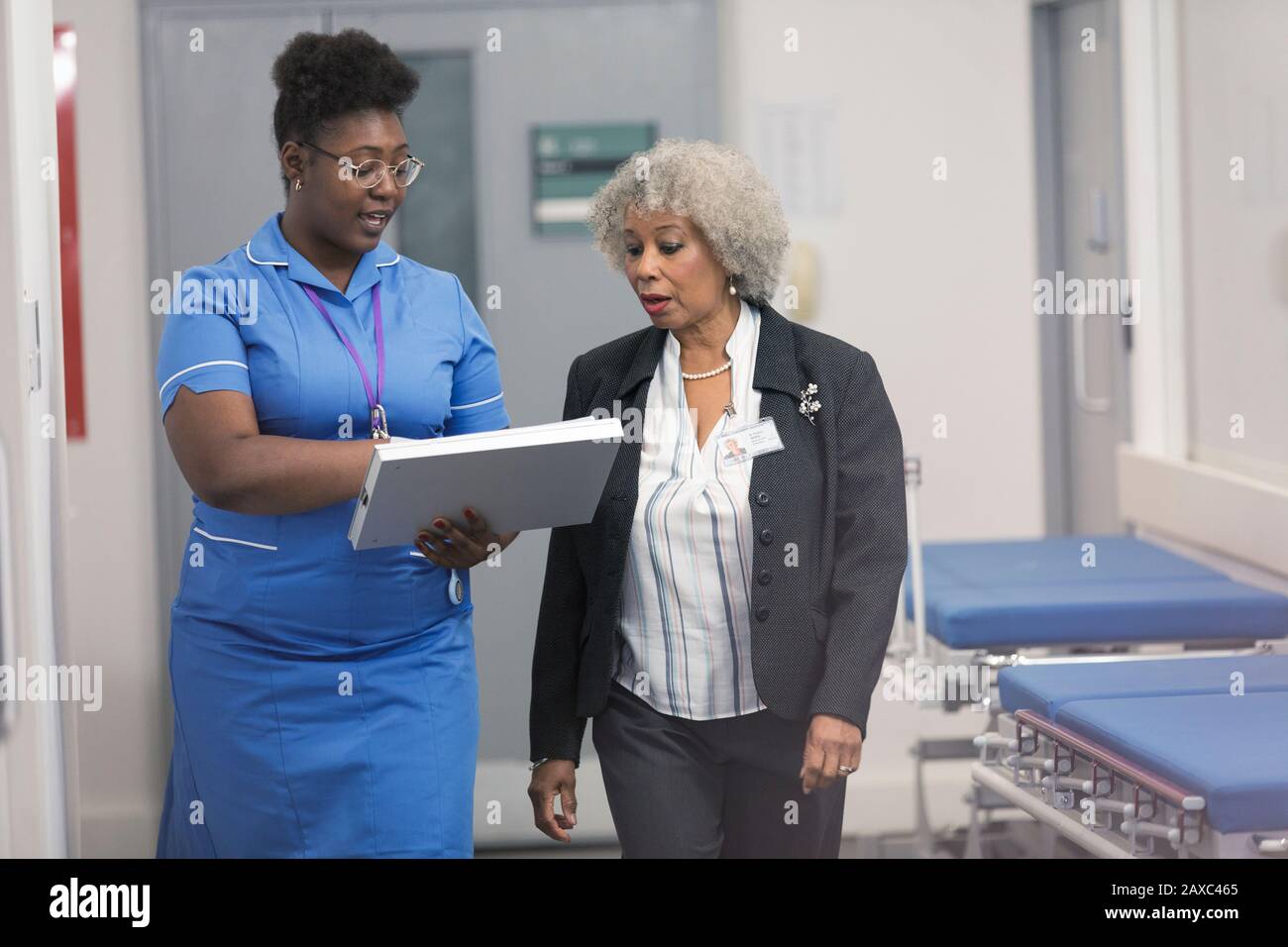 Female doctor and nurse discussing medical chart, making rounds in hospital corridor Stock Photo