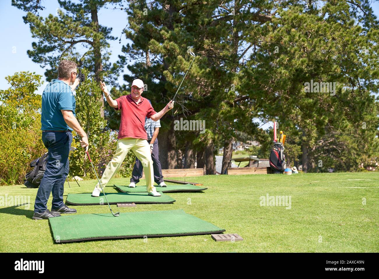 Happy senior male golfer cheering at sunny golf course driving range Stock Photo