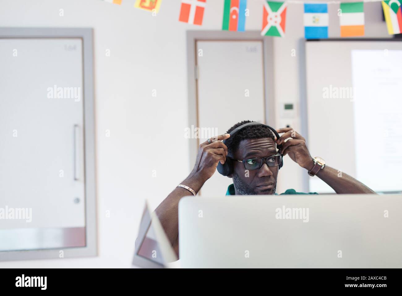 Mature male community college student adjusting headphones at computer in classroom Stock Photo