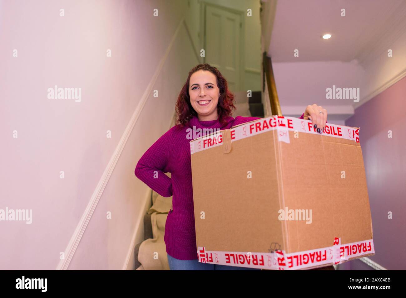 Portrait confident woman moving into new home, carrying cardboard box Stock Photo