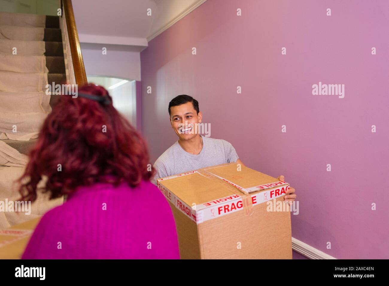 Happy couple moving into new house, carrying cardboard boxes up stairs ...