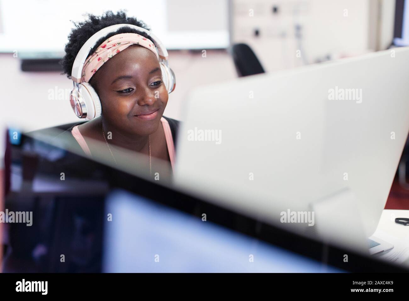 Smiling female community college student with headphones at computer in classroom Stock Photo