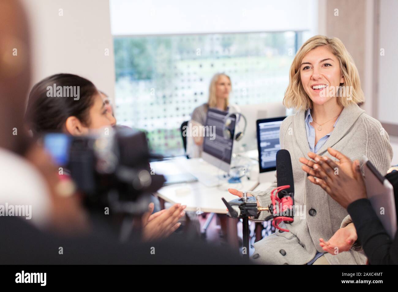 Classmates clapping for woman at microphone in journalism class Stock Photo
