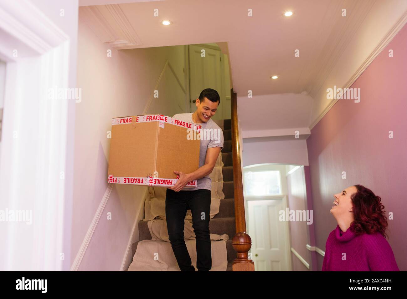 Happy couple moving out of house, carrying cardboard box down stairs Stock Photo