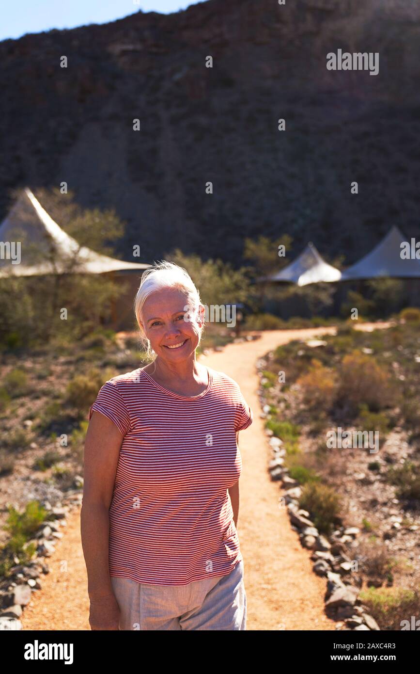 Portrait happy senior woman on footpath outside safari lodge cabins Stock Photo
