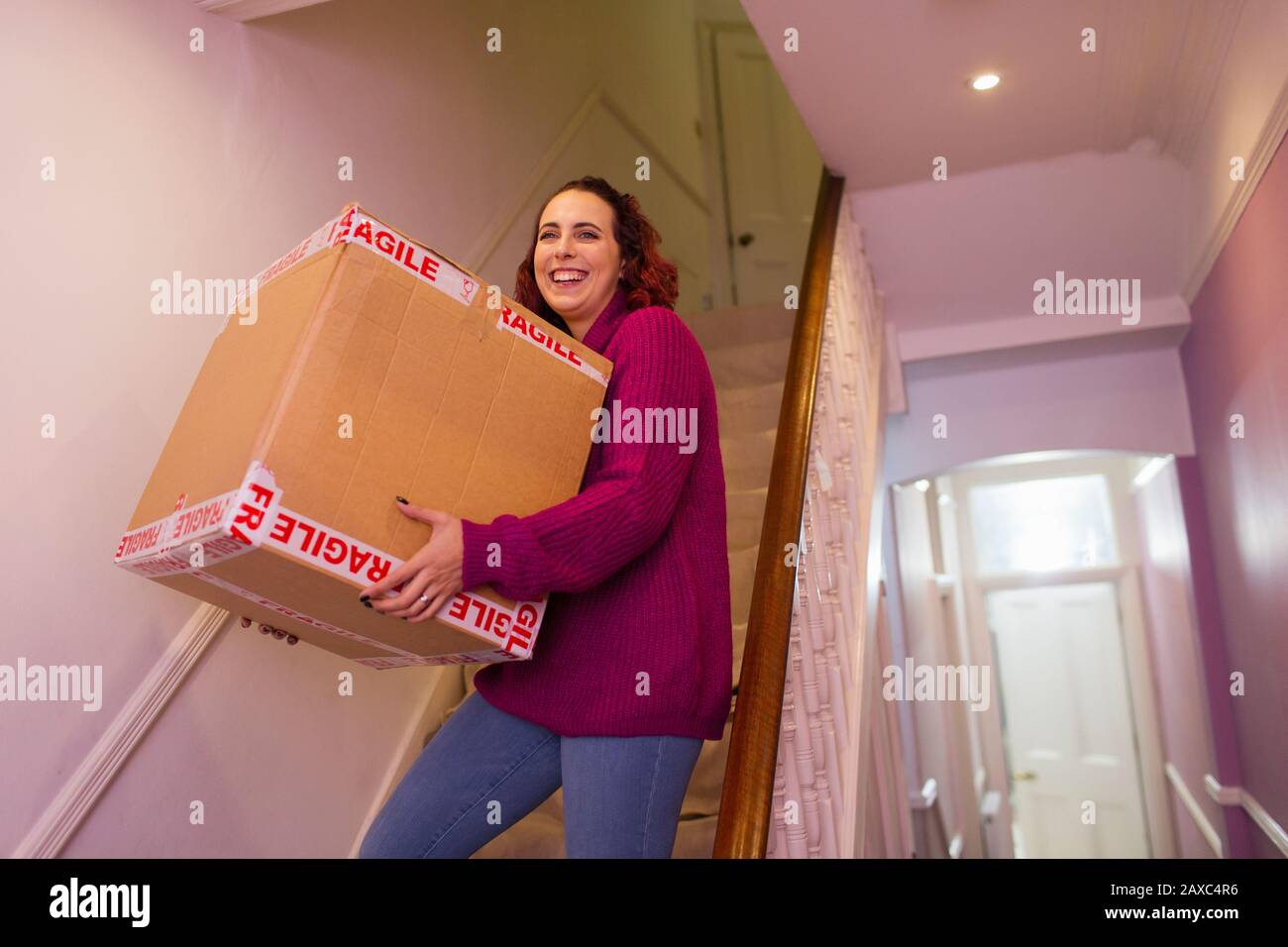 Portrait smiling woman moving house, carrying cardboard box on stairs Stock Photo
