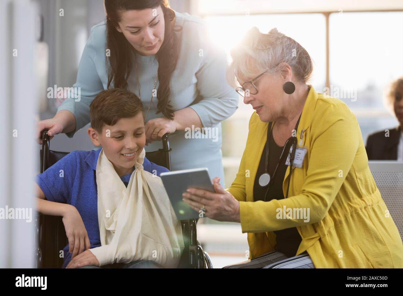 Doctor with digital tablet talking to boy patient in wheelchair and ...