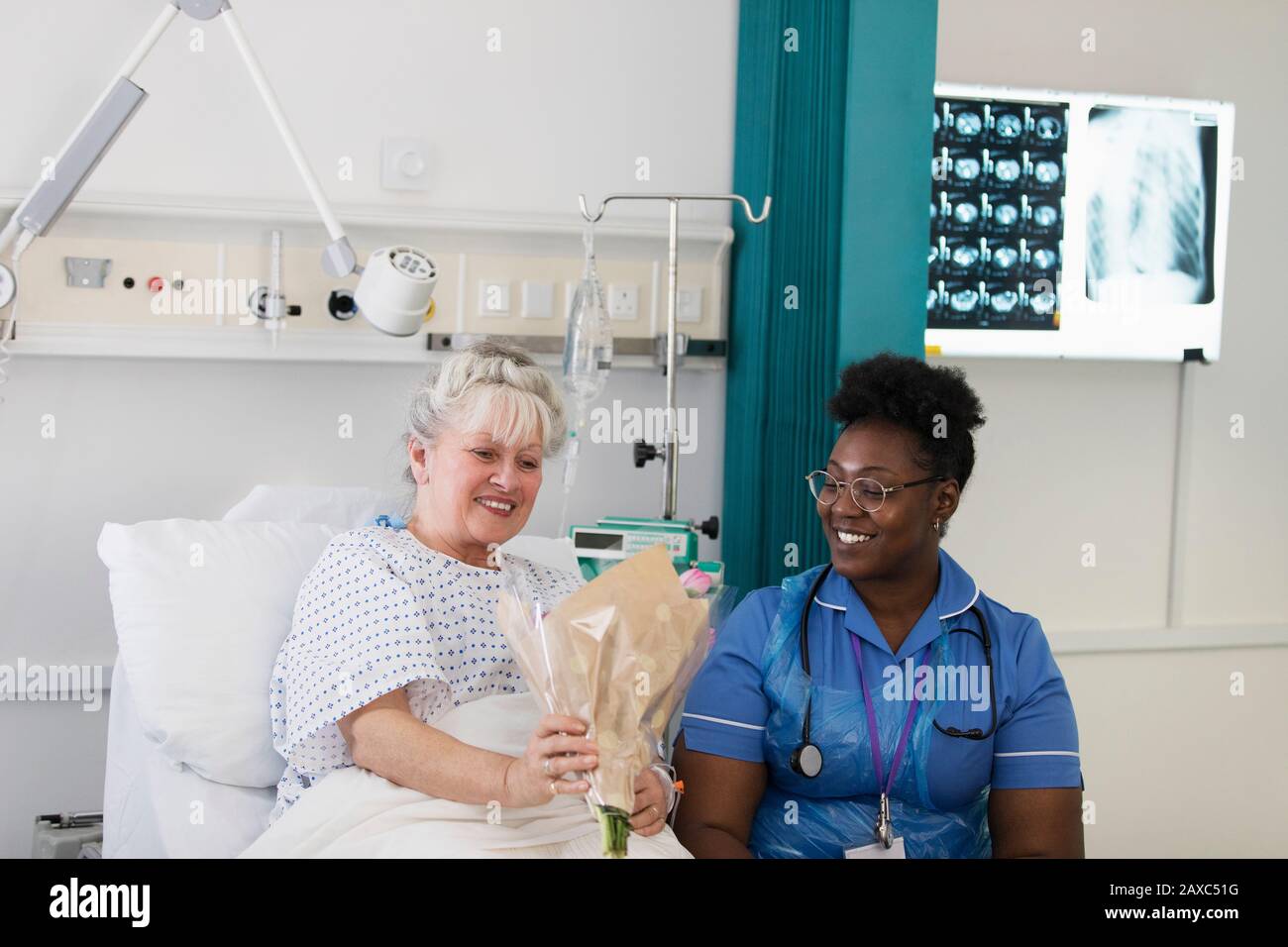 Female patient showing flowers to nurse in hospital room Stock Photo