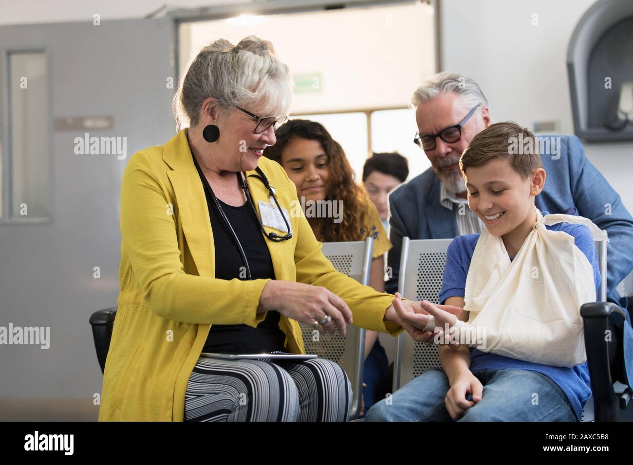 Female pediatrician examining hand of boy with arm in sling in clinic