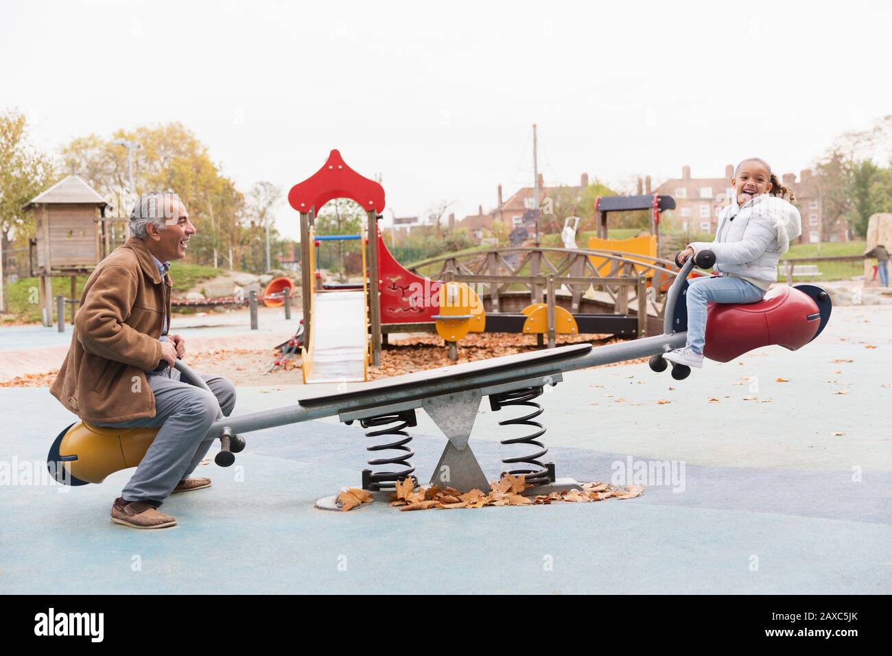 Grandfather and granddaughter playing on seesaw at playground Stock Photo