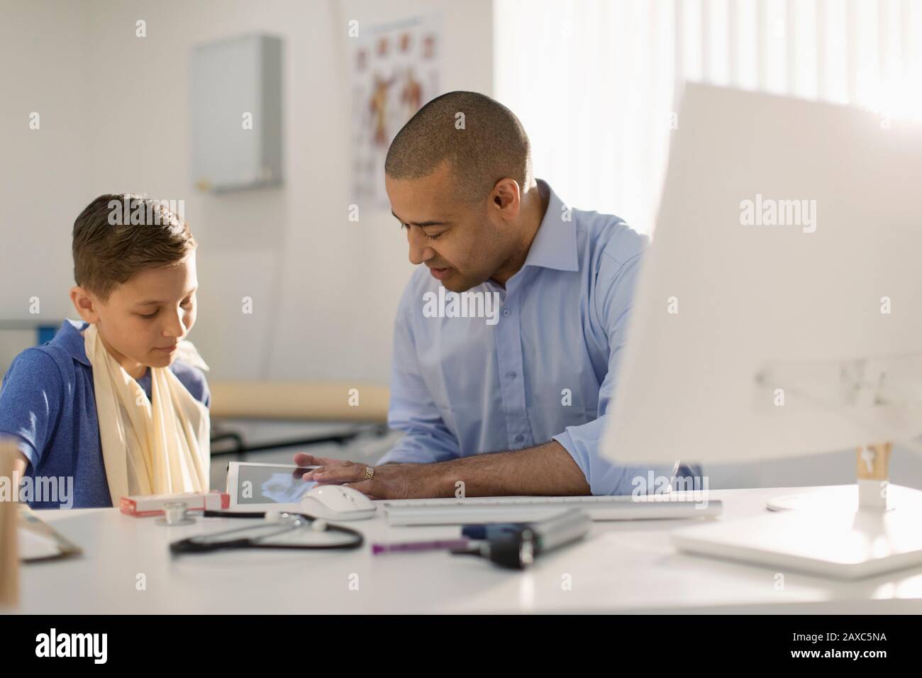 Male pediatrician showing digital x-ray to boy with arm in sling in doctors office Stock Photo