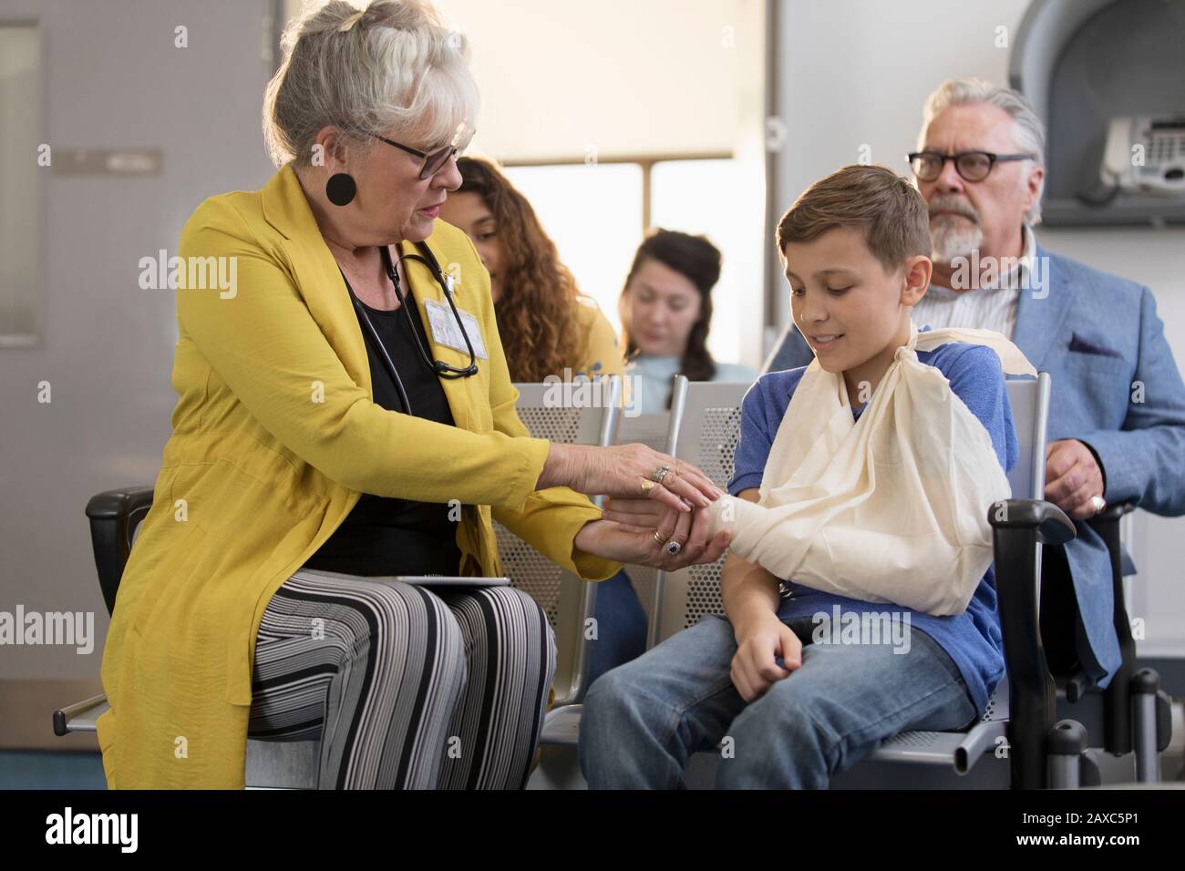 Female doctor examining hand of boy patient with arm in sling in clinic lobby Stock Photo
