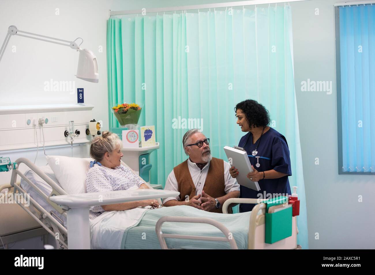 Doctor with medical chart making rounds, talking with senior couple in hospital room Stock Photo