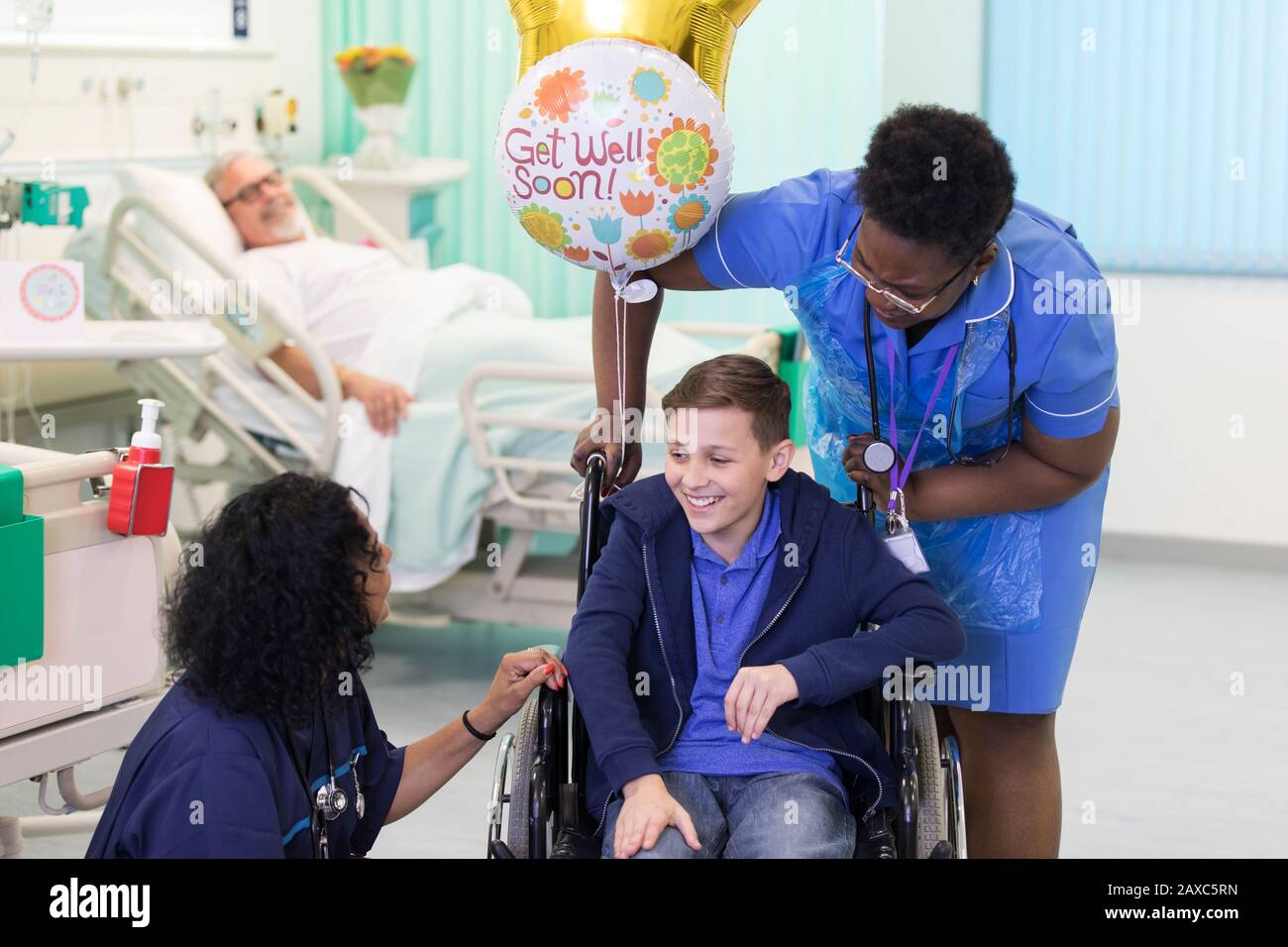 Doctor and nurse talking with boy patient in wheelchair in hospital ward Stock Photo