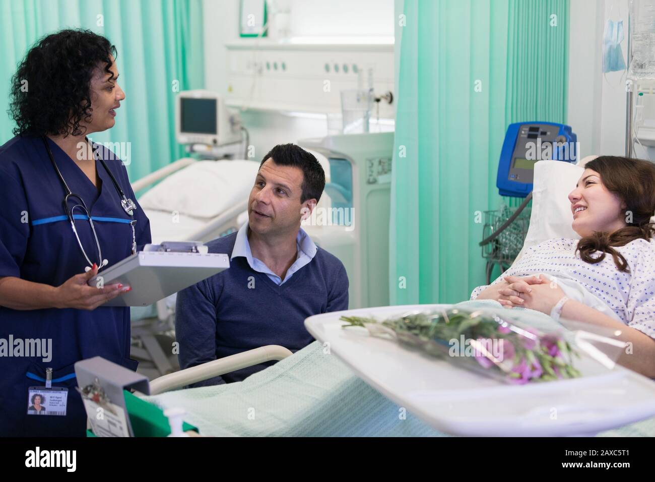 Doctor with medical chart making rounds, talking with couple in hospital room Stock Photo