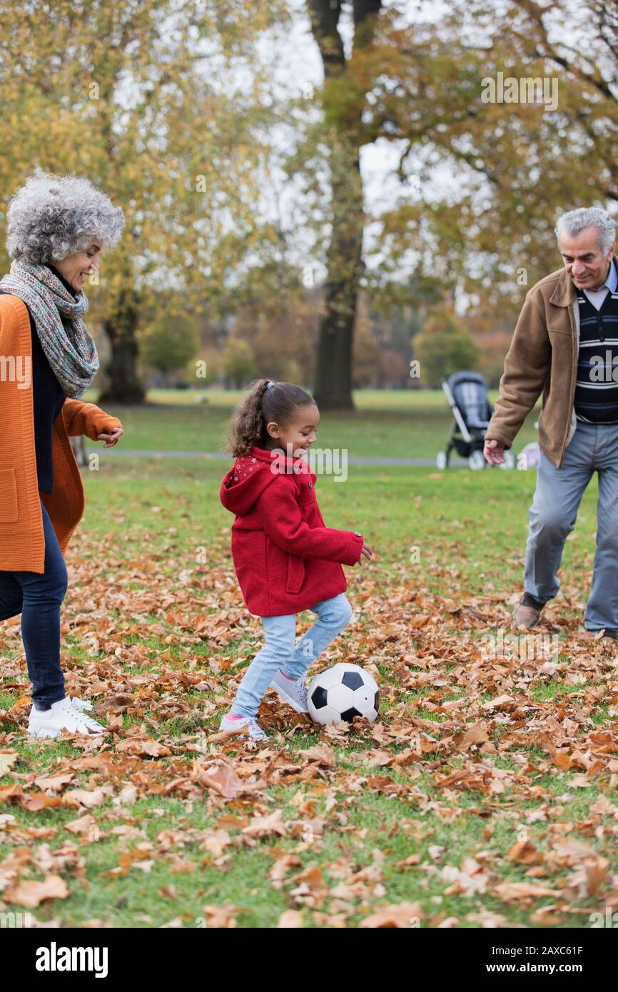 Grandparents playing soccer with granddaughter in autumn park Stock Photo