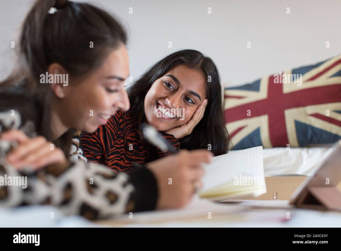 Smiling teenage girl friends studying doing homework on bed Stock Photo
