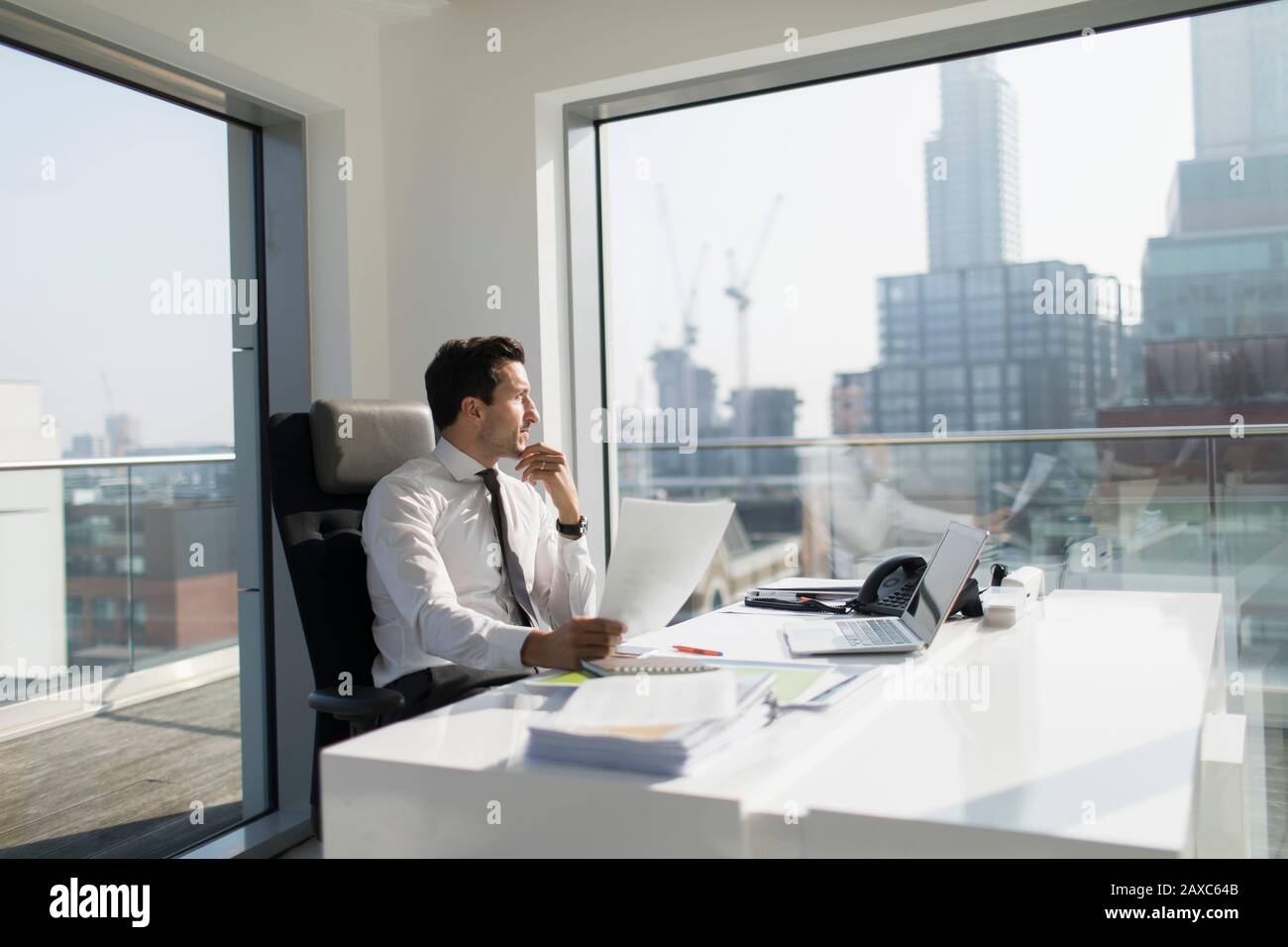 Thoughtful businessman with paperwork in sunny, modern, urban office Stock Photo