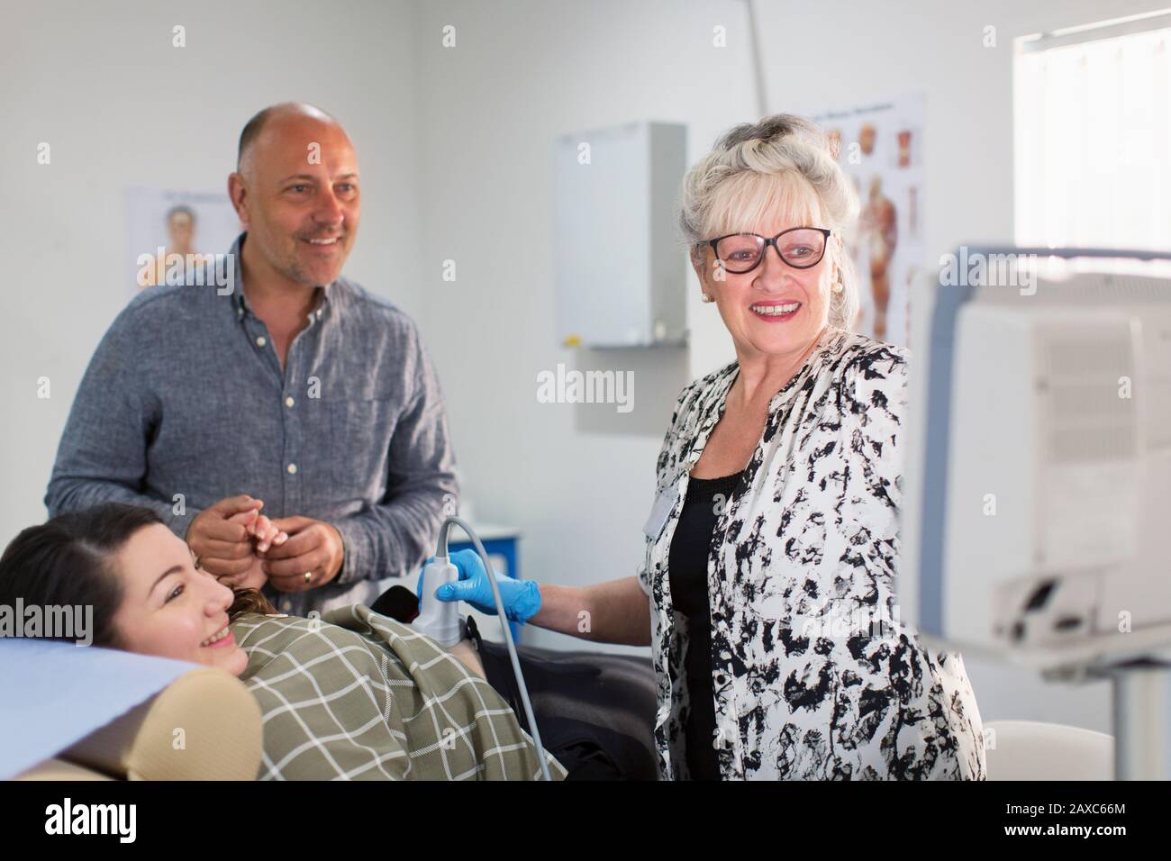Technician performing ultrasound for happy pregnant couple in examination room Stock Photo