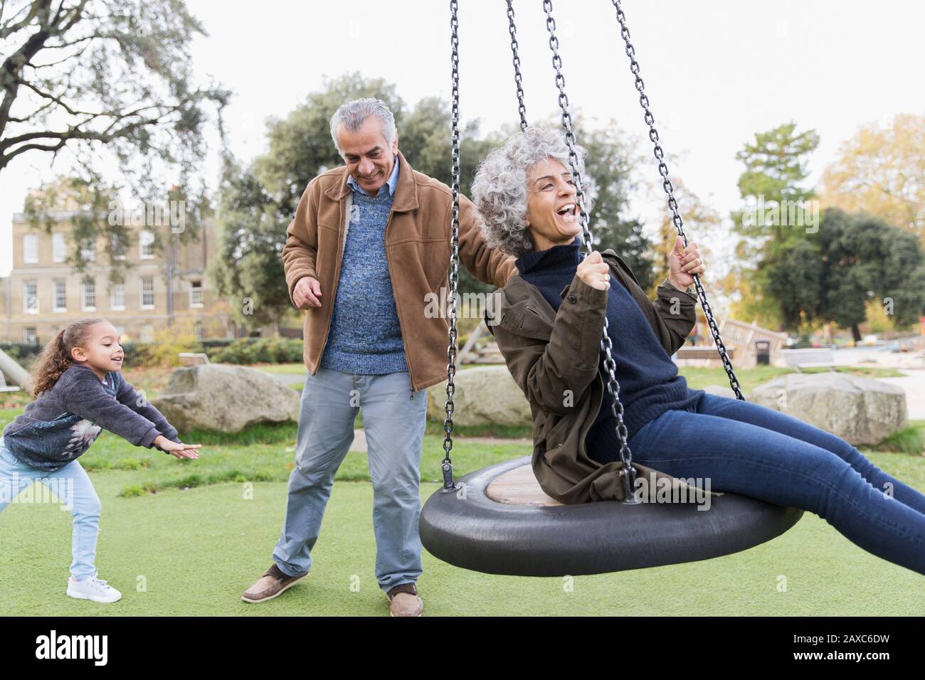 Playful grandparents and granddaughter playing on swing in park Stock Photo