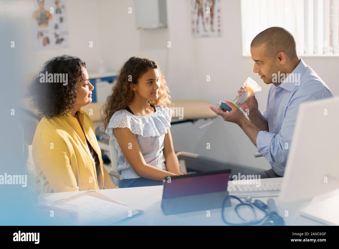 Male pediatrician teaching girl patient how to use inhaler in doctors office Stock Photo