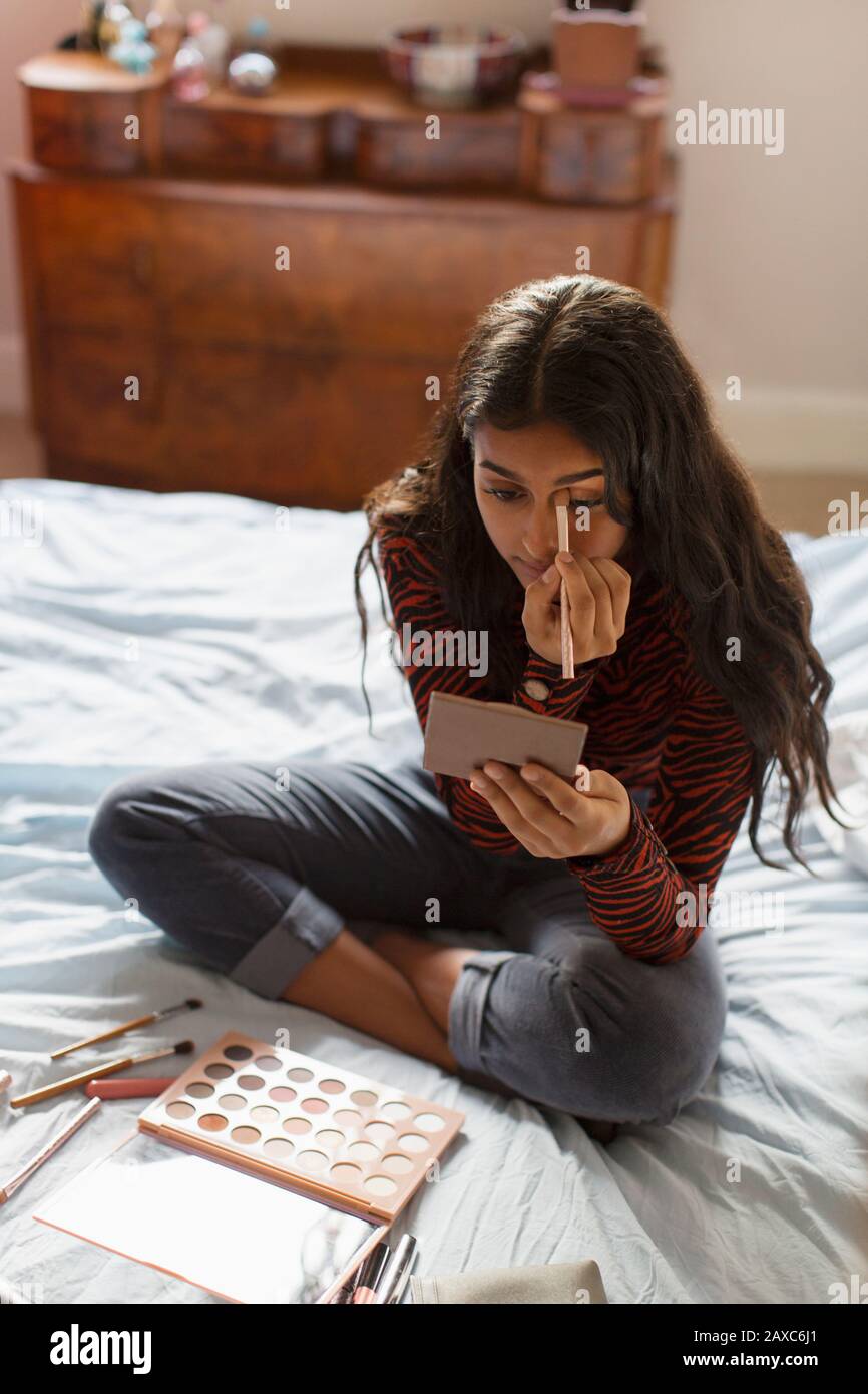 Teenage girl applying eyeshadow makeup on bed Stock Photo