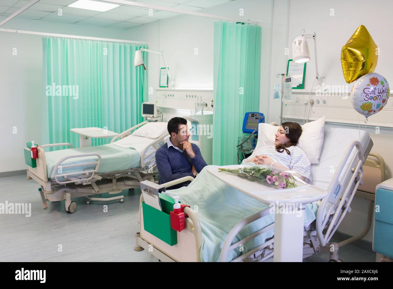 Man visiting, talking with wife resting in hospital ward Stock Photo