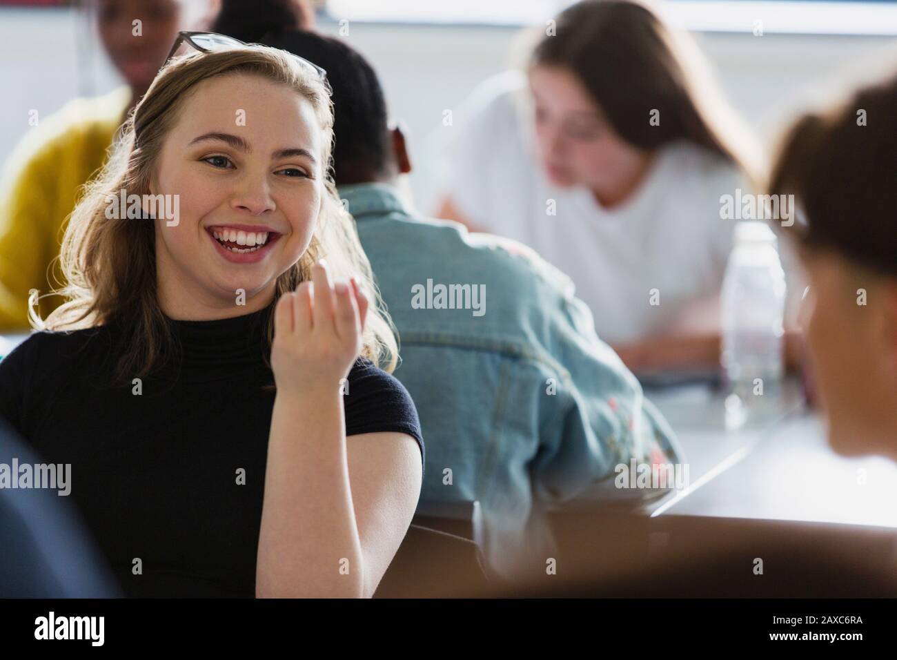 Happy, smiling high school girl student talking with classmate in classroom Stock Photo