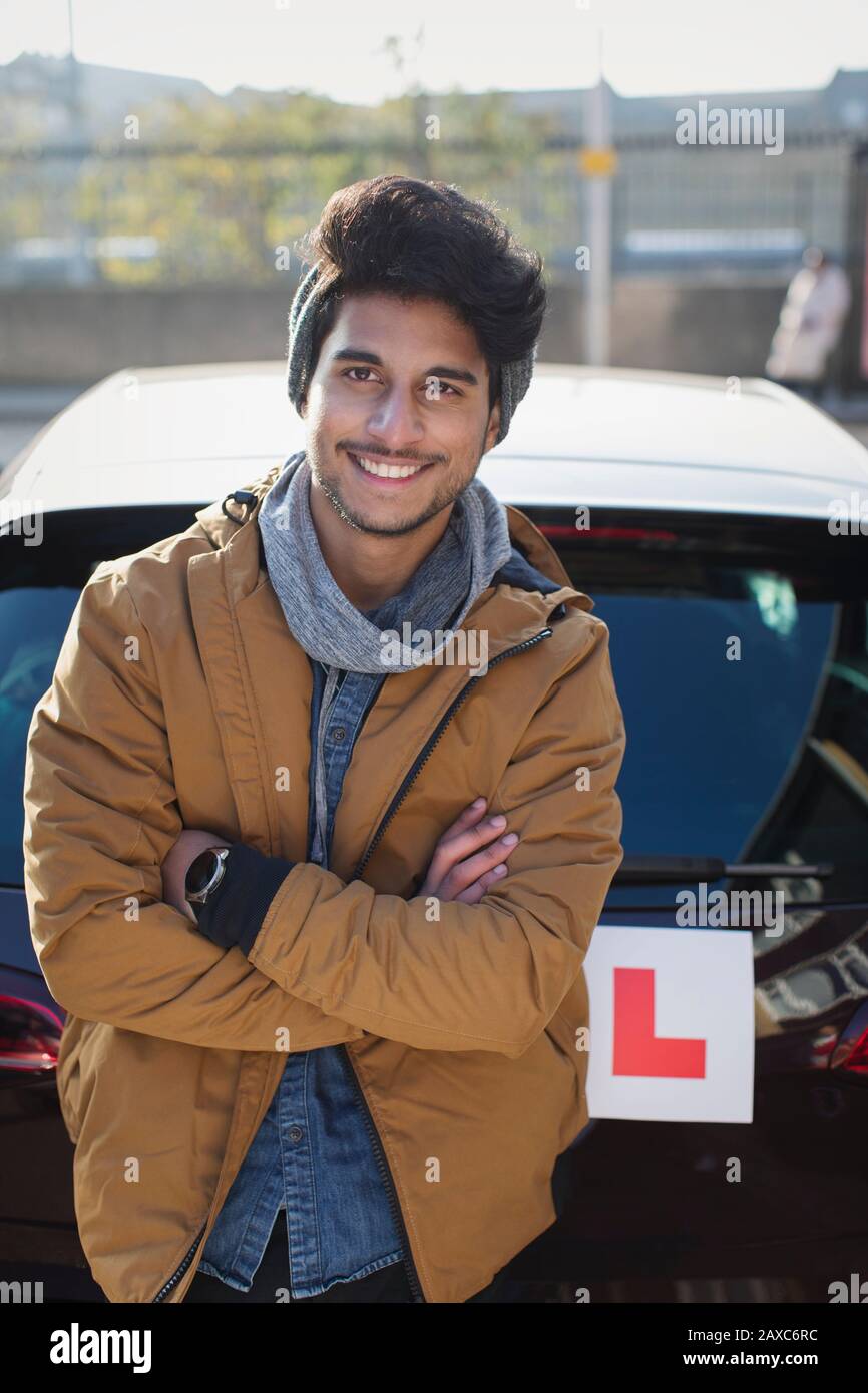 Portrait confident young man with learners permit leaning against car Stock Photo