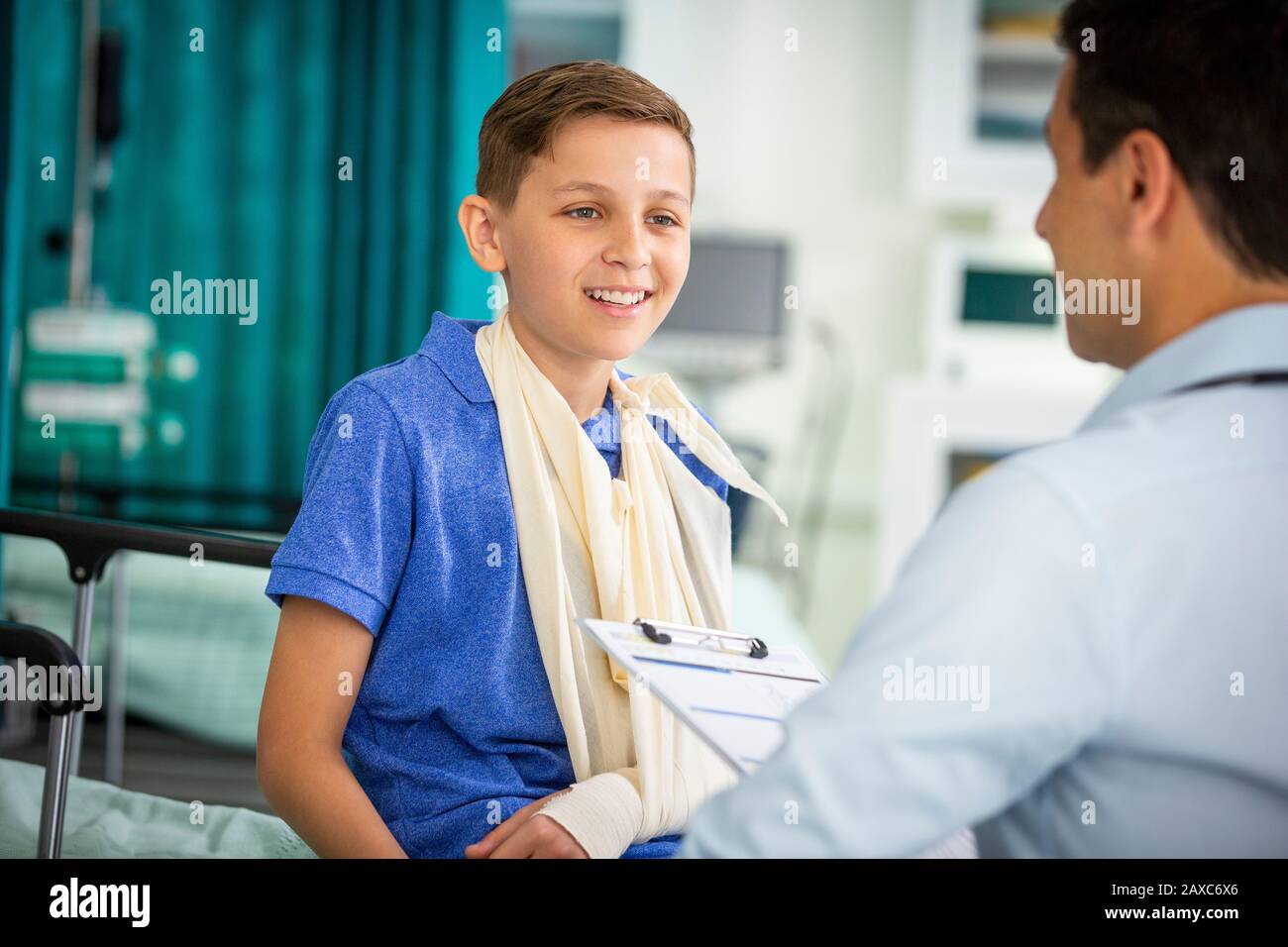Male pediatrician talking to boy patient with arm in sling in clinic Stock Photo