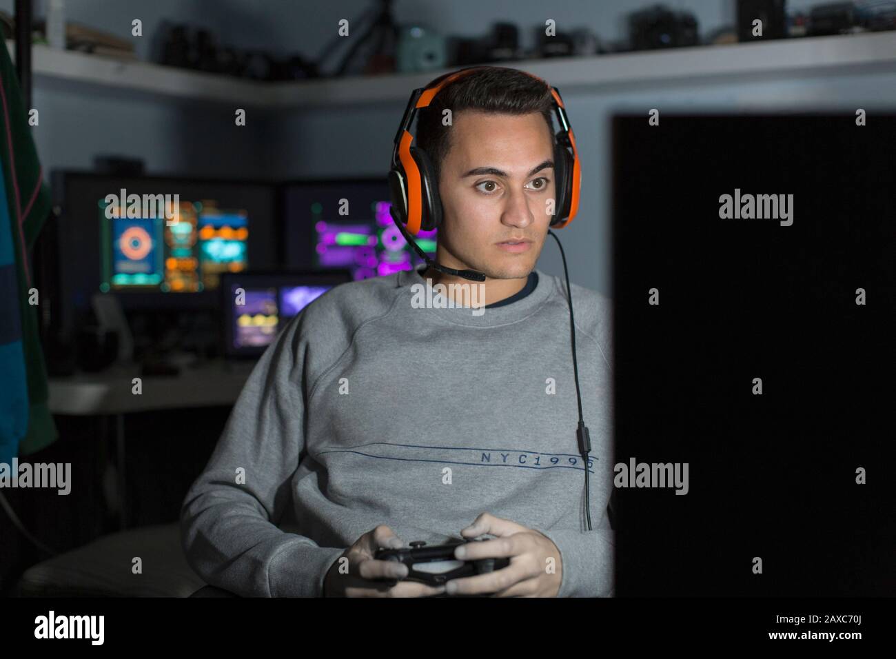 Focused teenage boy with headset playing video game at computer in dark