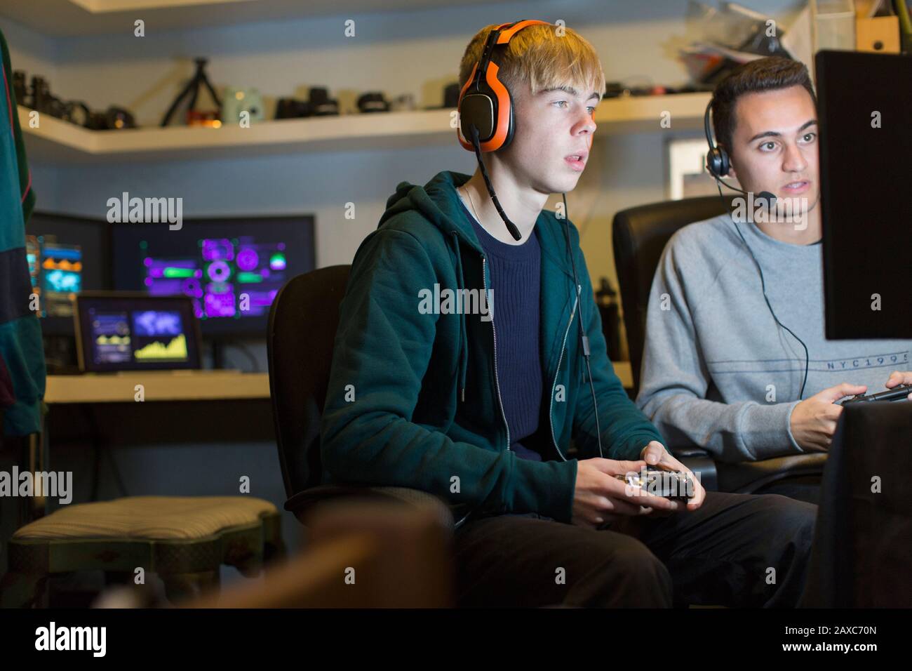 Teenage boys with headphones playing video game at computer in dark ...
