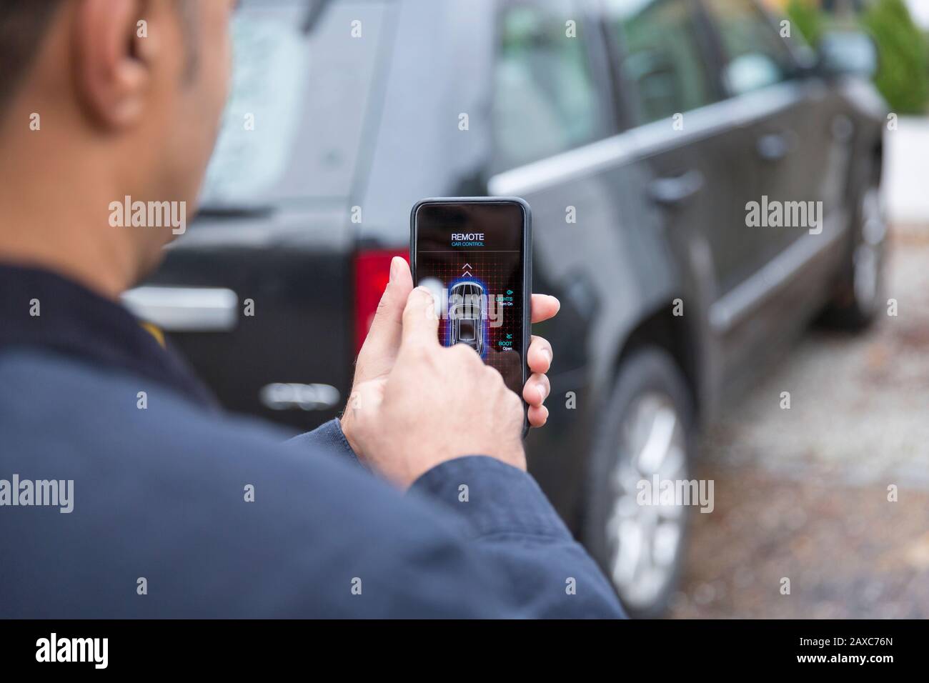 Man setting car alarm with smart phone in driveway Stock Photo