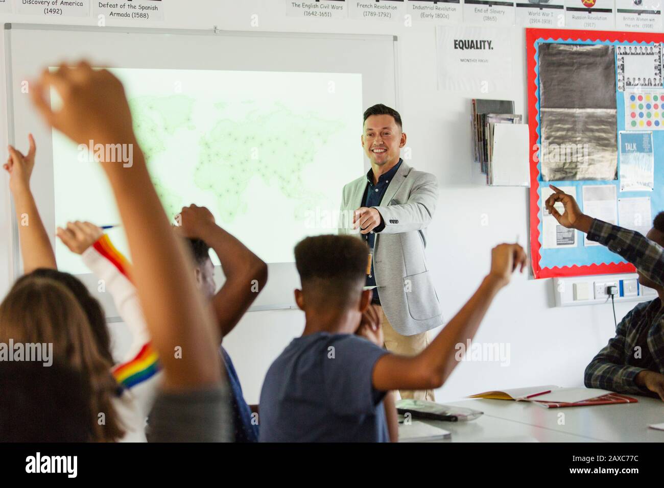 High school teacher leading lesson, calling on students with arms raised in classroom Stock Photo