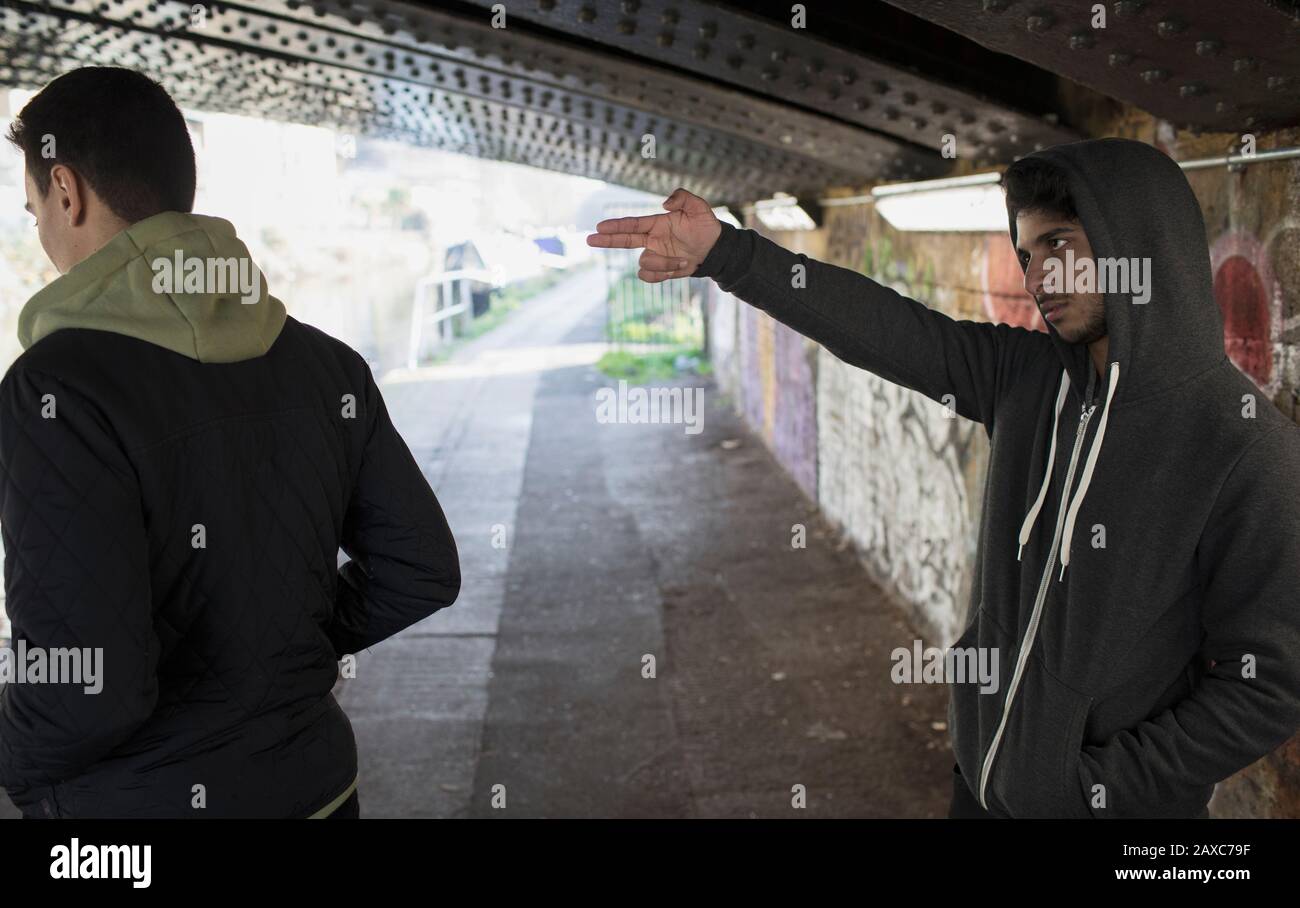 Menacing young man gesturing finger gun at man in urban tunnel Stock Photo
