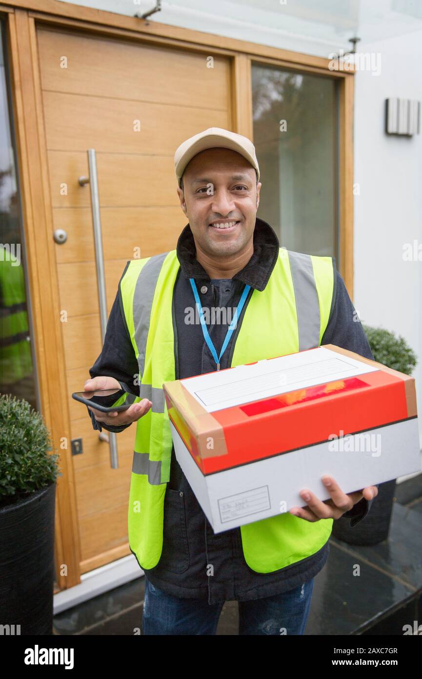 Portrait confident, friendly male deliveryman with smart phone at front door Stock Photo