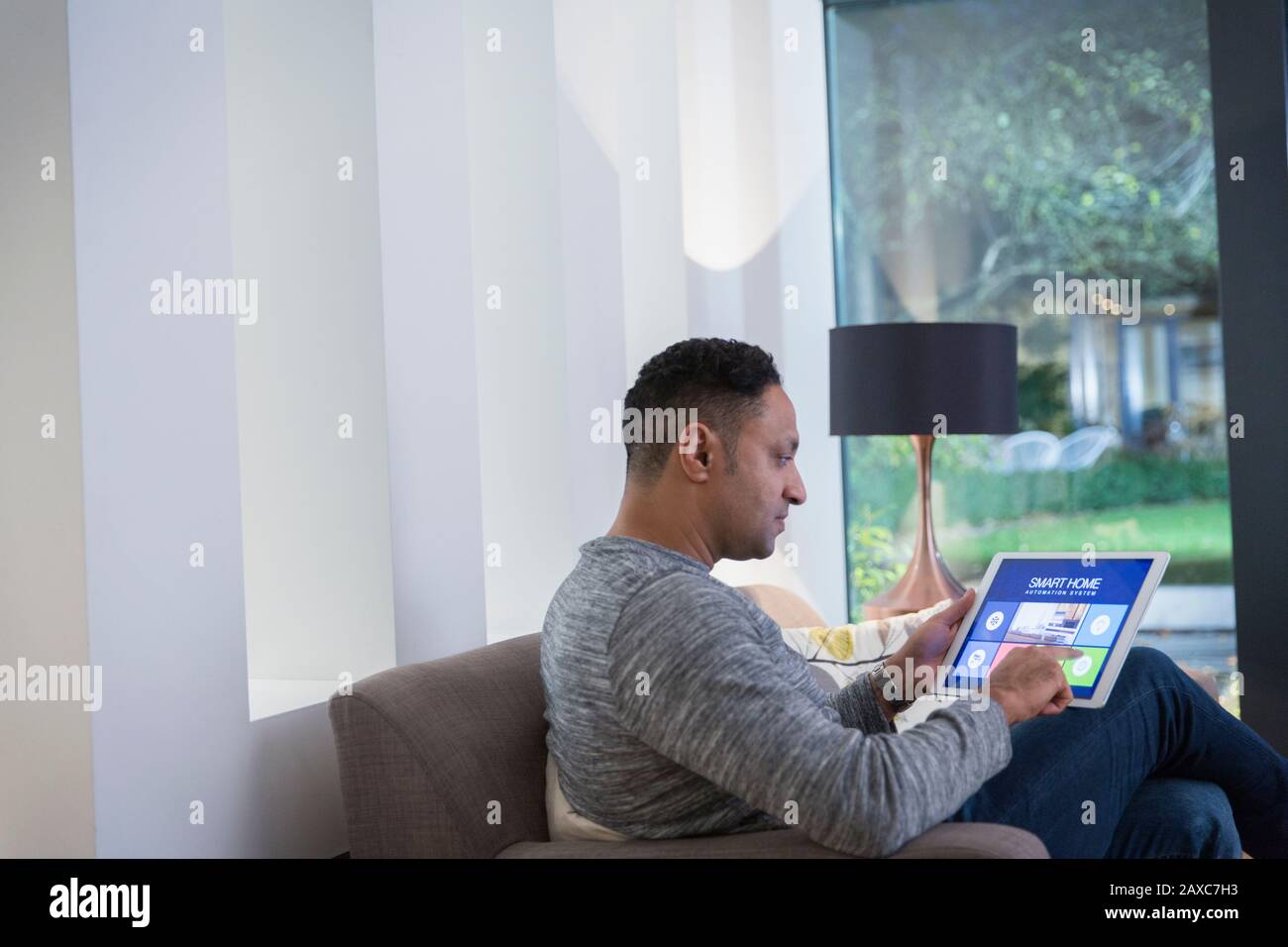 Man setting smart home alarm system from digital tablet on living room sofa Stock Photo