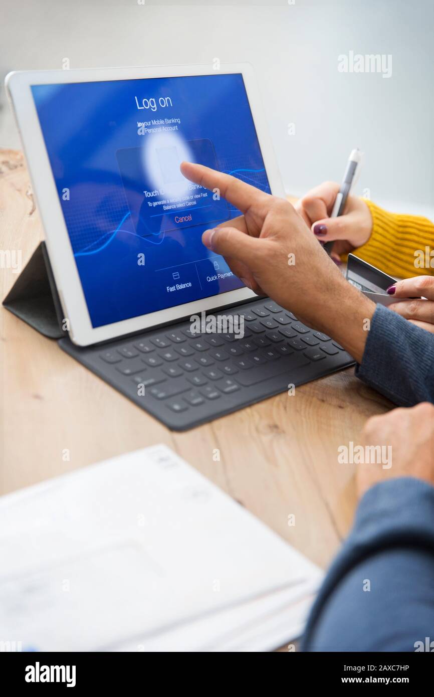 Couple paying bills, logging on to digital tablet with fingerprint Stock Photo