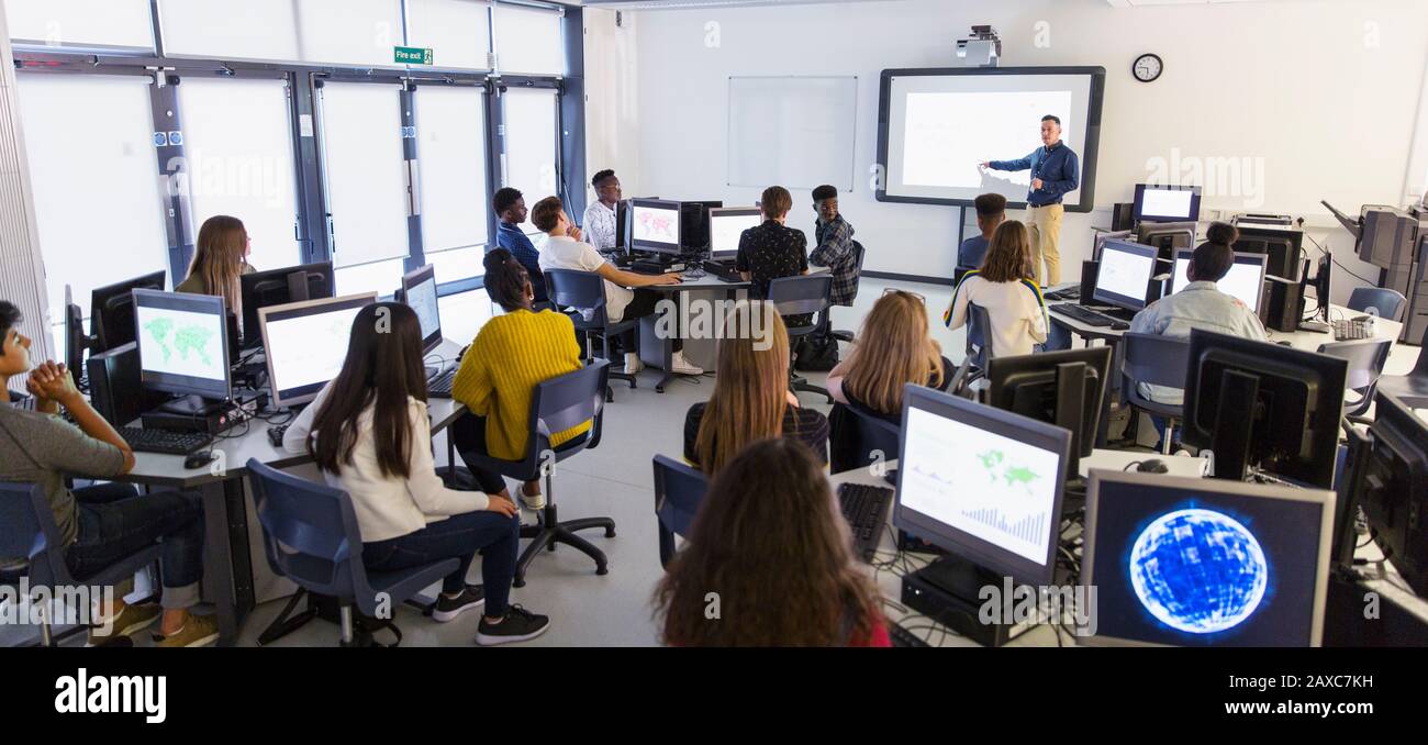 Junior high students using computers and watching teacher at projection screen in classroom Stock Photo
