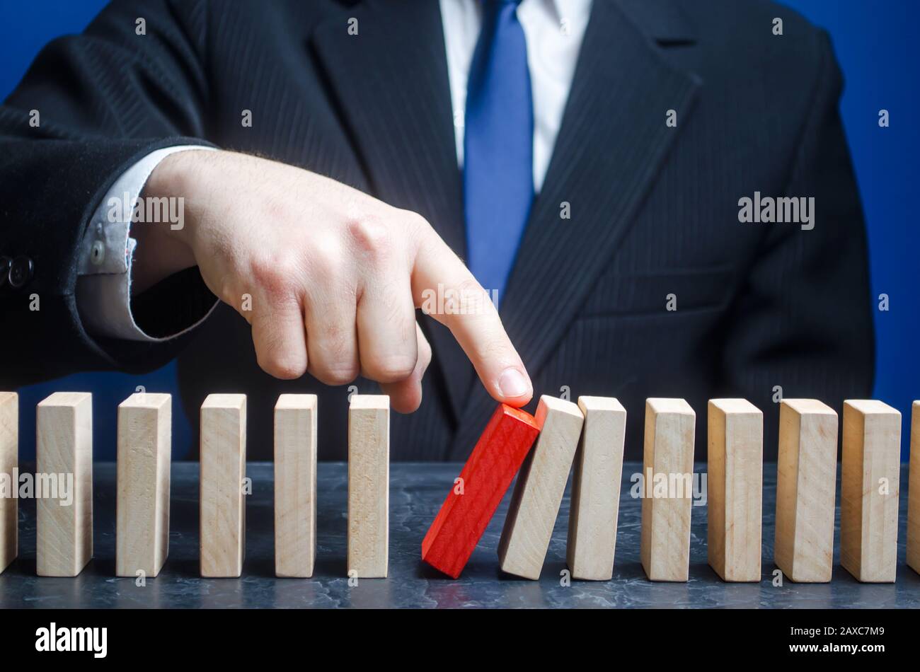 Businessman starts the process of falling dominoes. Starting work after stopping. Continuation of working, obstacle avoidance. maintainability. Correc Stock Photo