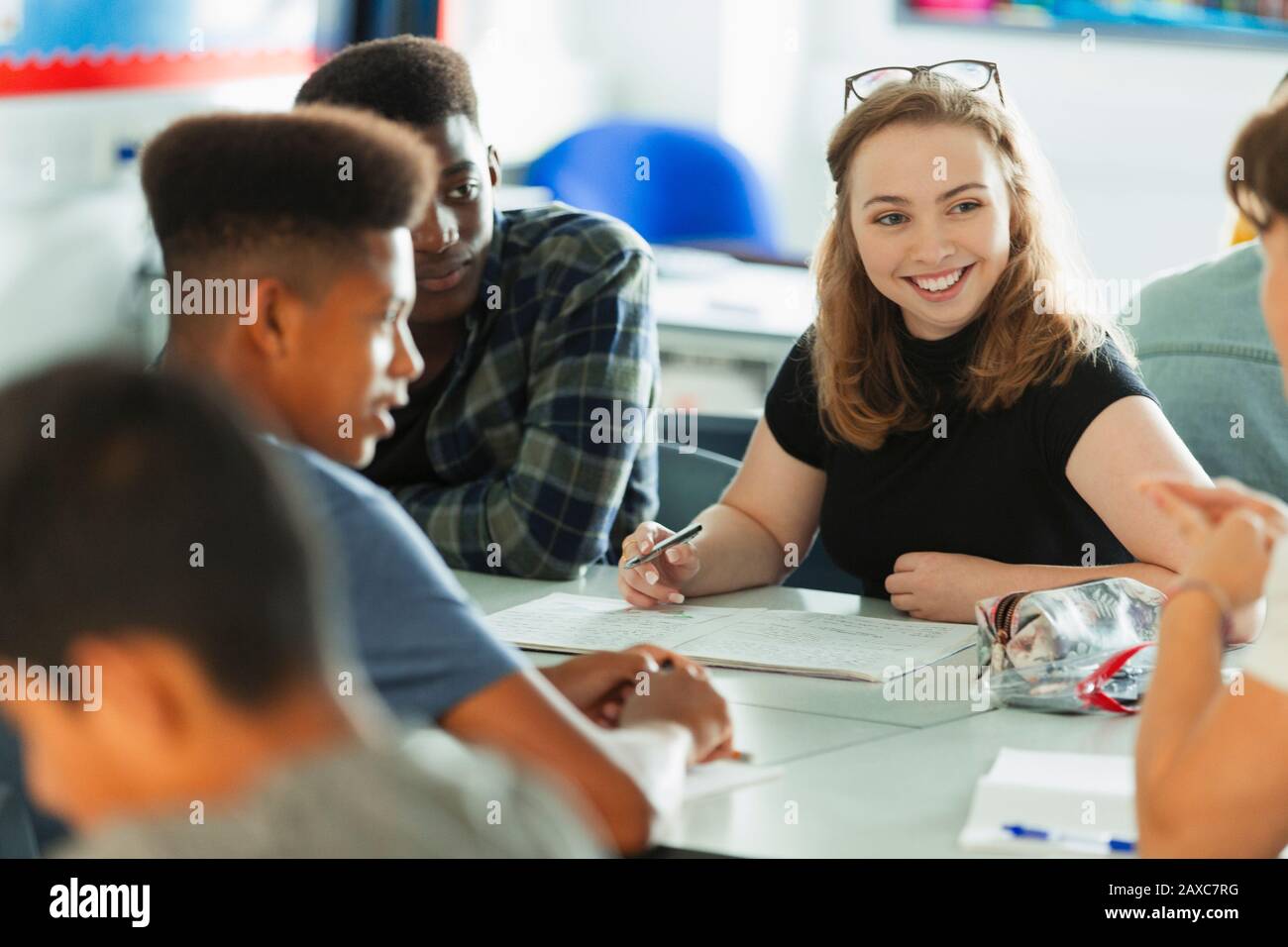 Smiling high school girl student talking with classmates in classroom Stock Photo