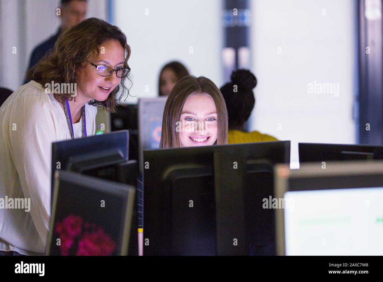 Female junior high teacher helping girl student at computer in computer lab Stock Photo