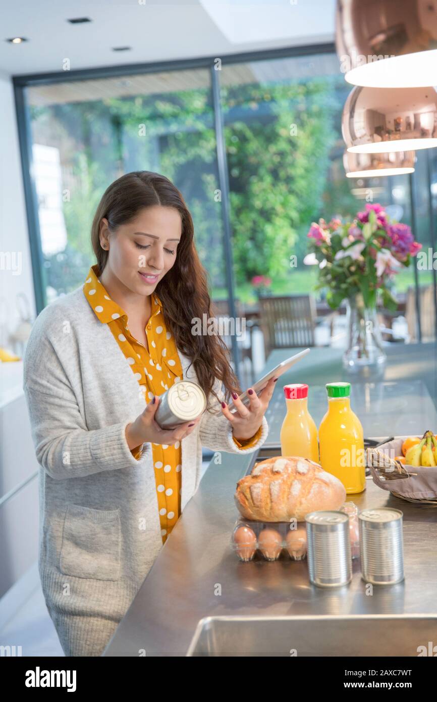 Woman with digital tablet checking food labels in kitchen Stock Photo