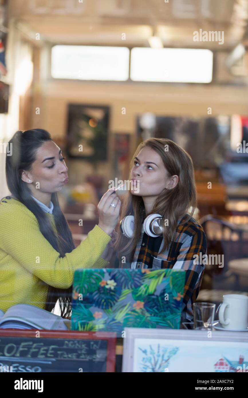 Young women applying lip gloss in cafe window Stock Photo