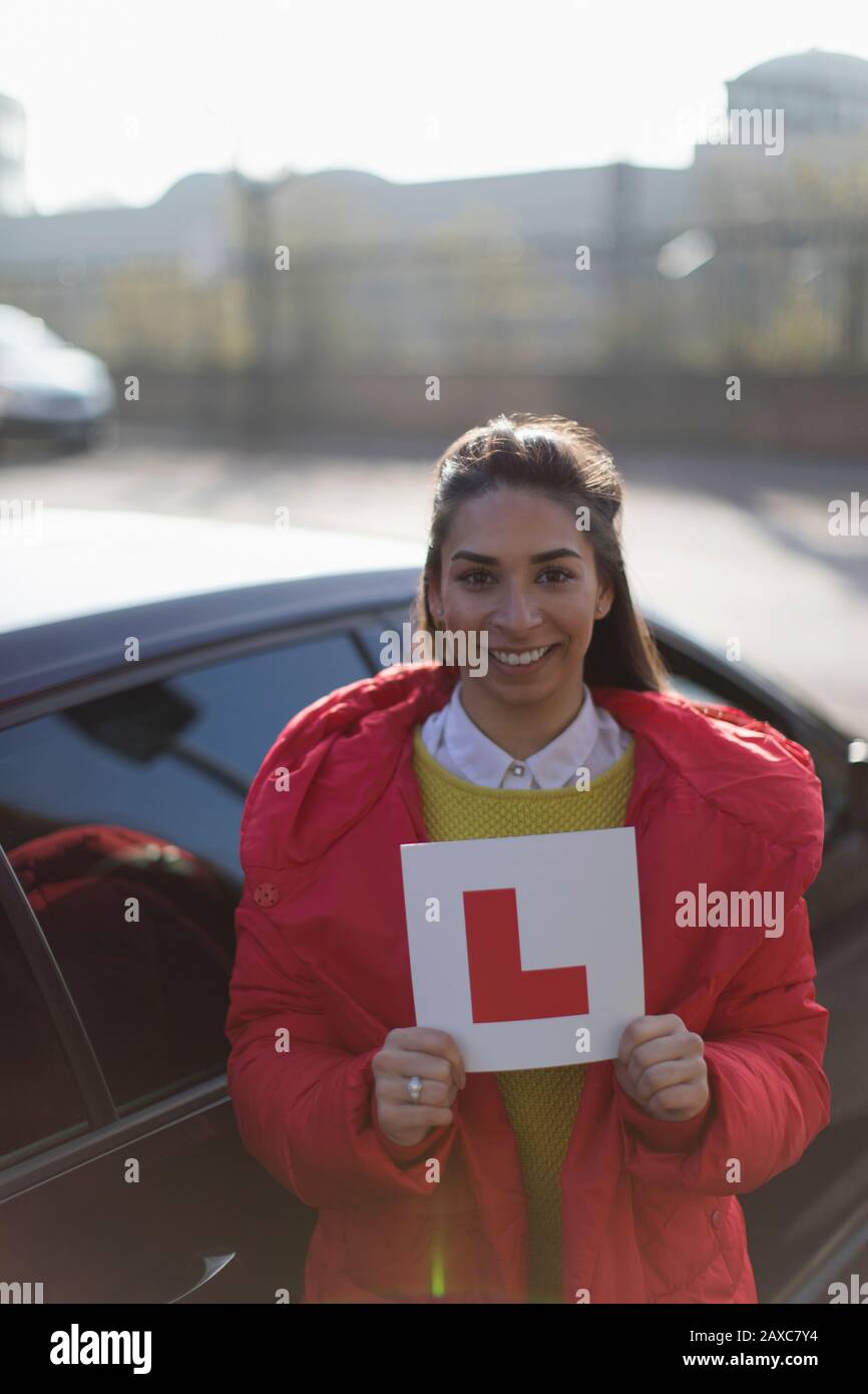 Portrait happy young woman holding learner permit next to car Stock Photo
