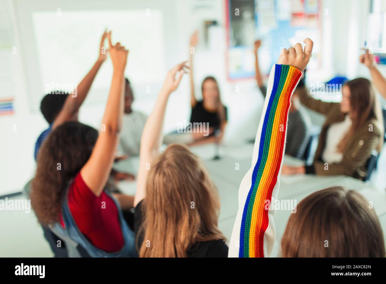High school students with arms raised, asking questions in classroom Stock Photo