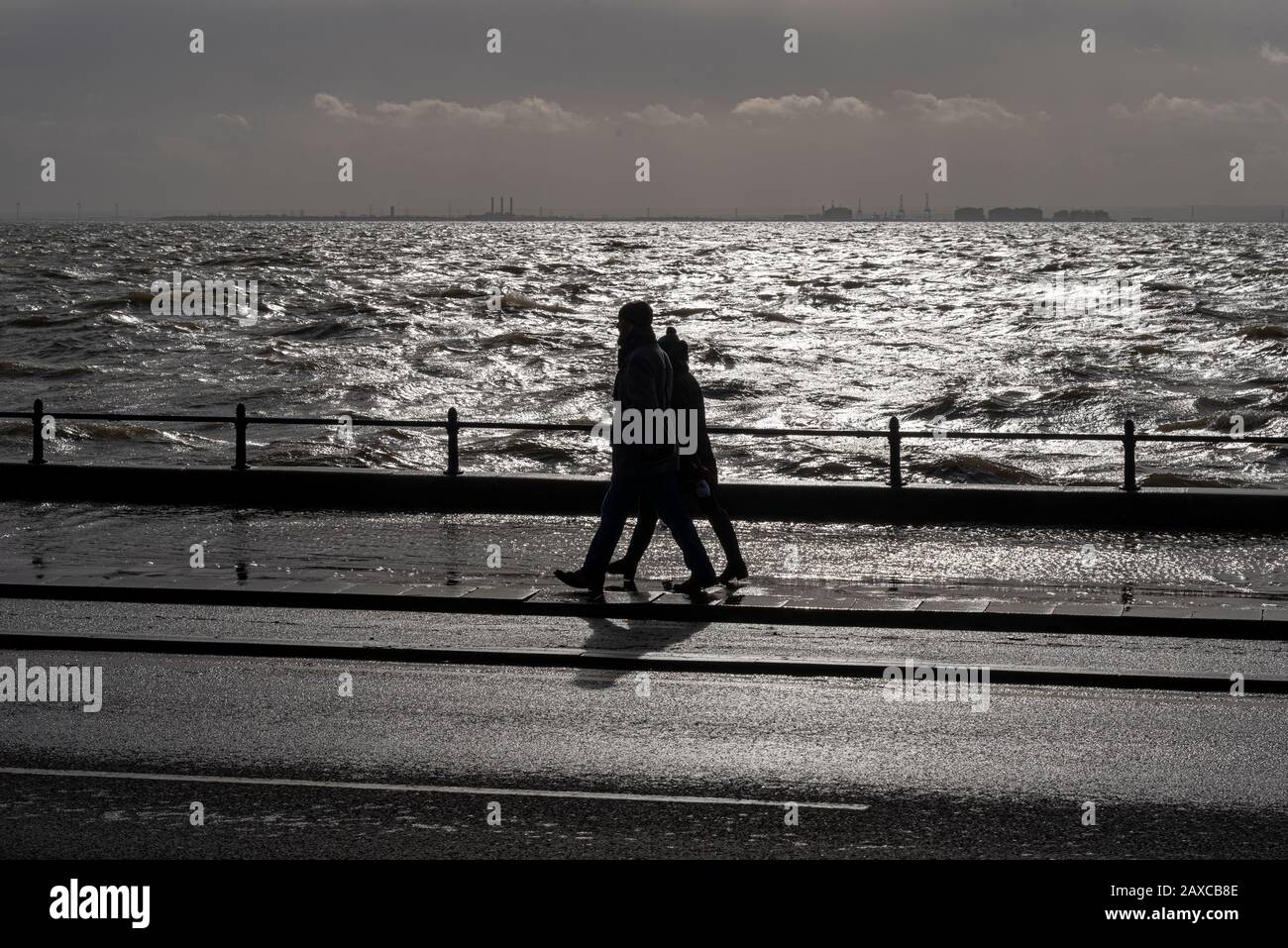 Male and female couple walking along Western Esplanade of Southend on Sea, Essex, UK passing flooded pavement during storm surge of storm Ciara Stock Photo